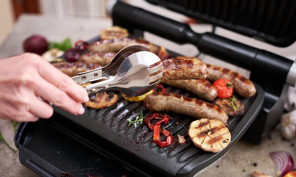 Henkilö grillaa lihaa ja kasviksia sähkögrillillä