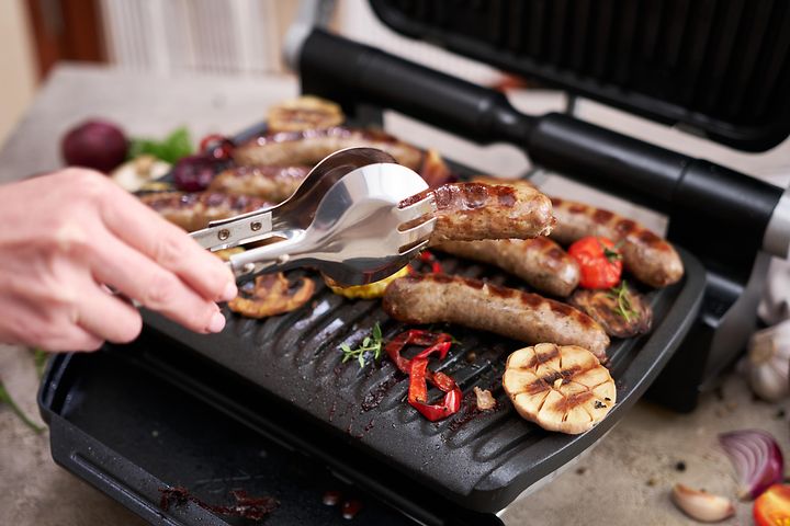Henkilö grillaa lihaa ja kasviksia sähkögrillillä
