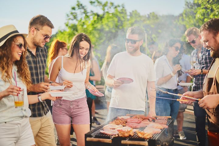 Joukko ystäviä on kerääntynyt grillaamaan ulkona aurinkoisessa säässä