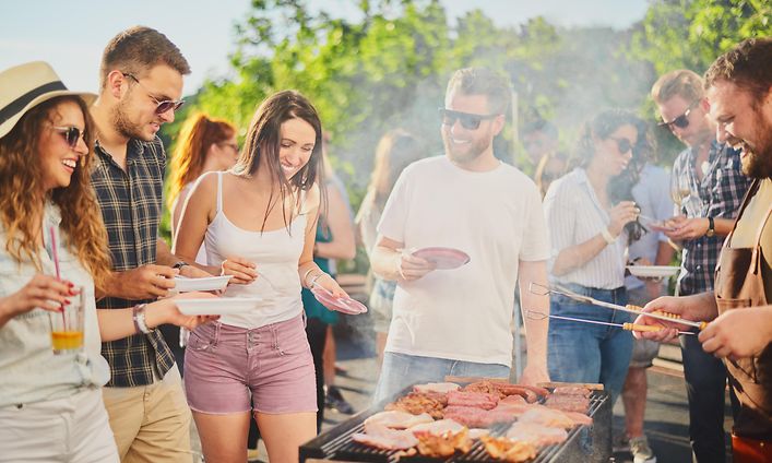 Joukko ystäviä on kerääntynyt grillaamaan ulkona aurinkoisessa säässä