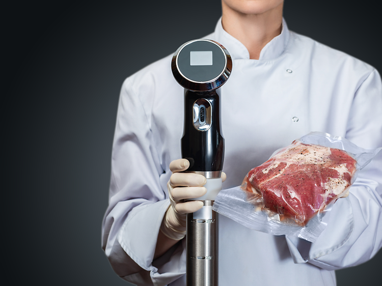 Sous Vide - Kokki pitää käsissään tyhjiöpakattua lihaa- ja sous vide -kiertovesipumppua