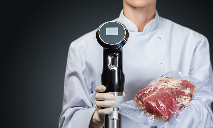 Sous Vide - Kokki pitää käsissään tyhjiöpakattua lihaa- ja sous vide -kiertovesipumppua