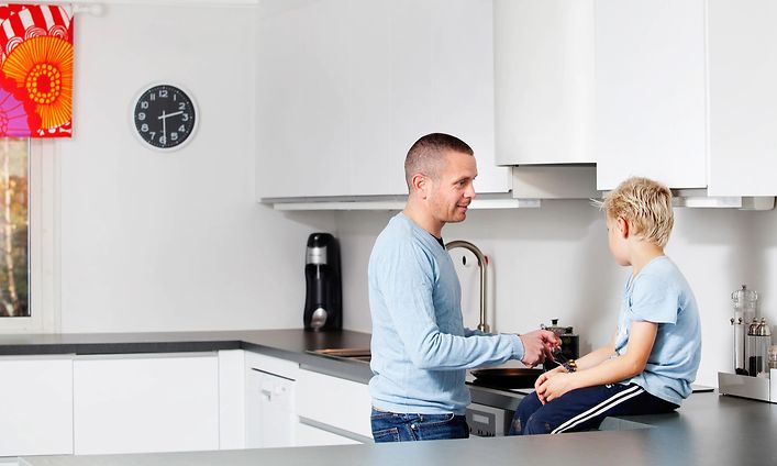 Mies laittaa ruokaa pojan istuessa keittiön työtasolla