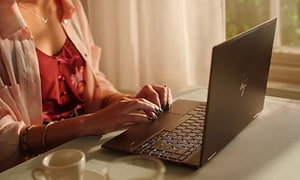 nainen kirjoittamassa HP:n kannettavalla tietokoneella kahvikuppi vieresssään