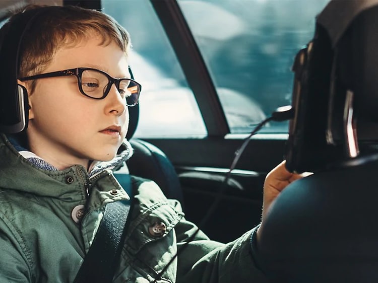 Poika istuu auton takapenkillä käyttäen etuistuimen takaosaan kiinnitettyä tablettia