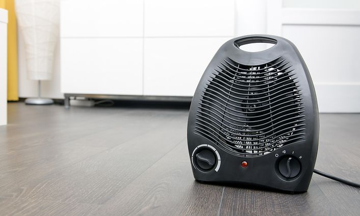 Musta lämpöpuhallin lattialla valkoisen lipaston edessä