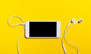 Valkoinen iPhone ja nappikuulokkeet keltaista taustaa vasten
