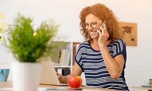 kannettavan tietokoneen ääressä istuva nainen puhumassa puhelimeen