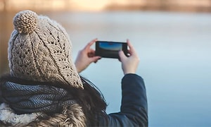 Talvivaatteisiin pukeutunut nainen ottamassa maisemakuvaa älypuhelimella