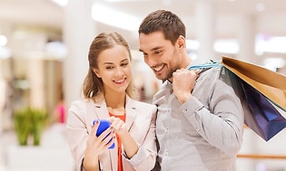 Pariskunta ostoksilla kauppakeskuksessa, nainen näyttää jotain puhelimessaan