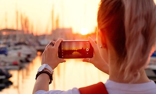 Nainen ottaa valokuvan auringonlaskun aikaan satamassa