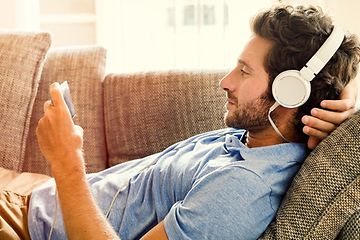 Mies rentoutumassa sohvalla puhelin kädessään kuulokkeet korvillaan
