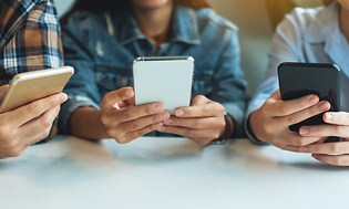 kolme teini-ikäistä käyttämässä älypuhelimiaan