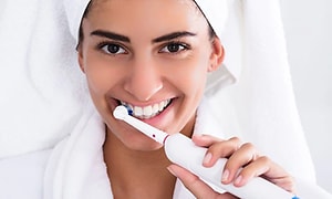 Nainen harjaamassa hampaitaan valkoisella sähköhammasharjalla