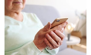 vanhempi naishenkilö istumassa älypuhelin kädessään