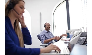 Työntekijöitä, joilla on kuulokkeet päässään avoimessa toimistoympäristössä