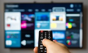 TV-kaukosäädin kädessä, taustalla älytelevisio