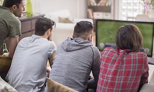 4 men on a sofa watching football on small TV