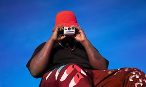 Mies punaisessa hatussa pitää Polaroid Go-kameraa kasvojensa edessä